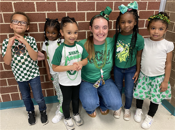 photo of students gathered around a staff member as they are all wearing green.